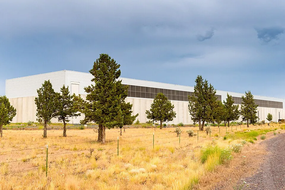 A long, low data centre building behind pine trees and dry grass in Prineville, Oregon