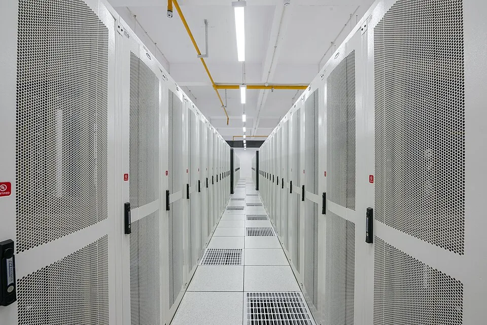 A long, bright aisle between rows of white server cabinets in a data centre