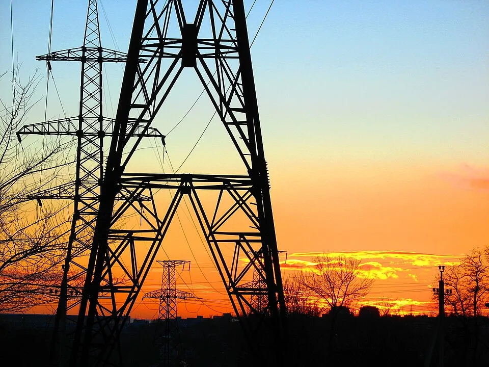 Electricity pylons silhouetted against an orange sunset