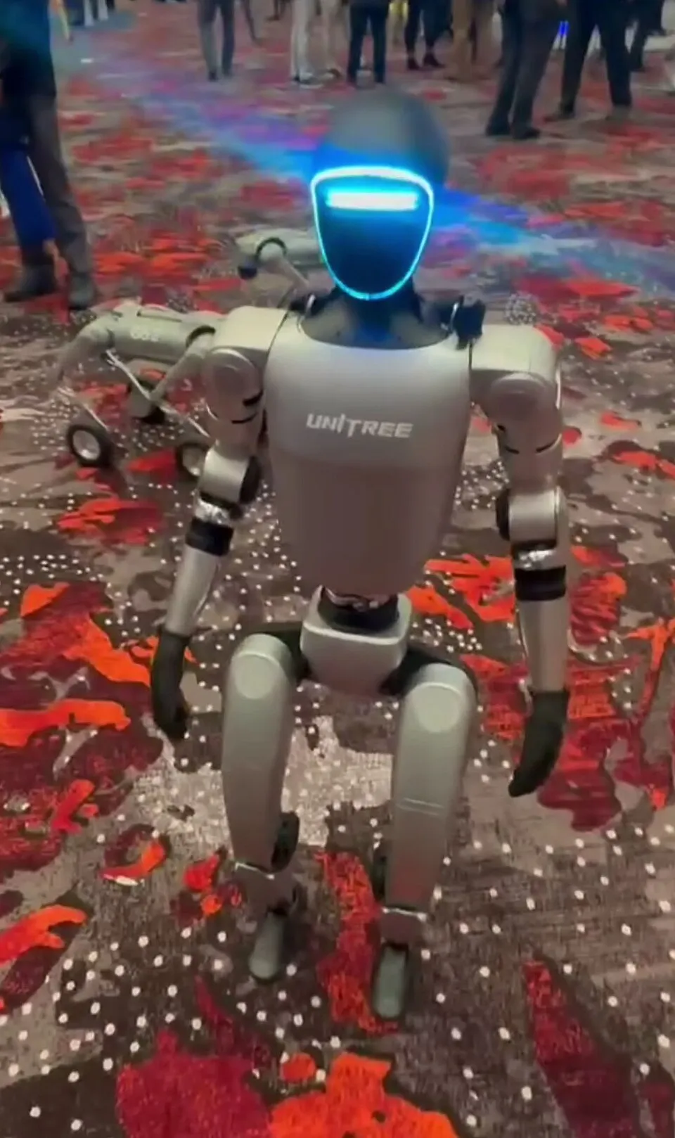A Unitree G1 humanoid robot with a glowing face standing at a trade show