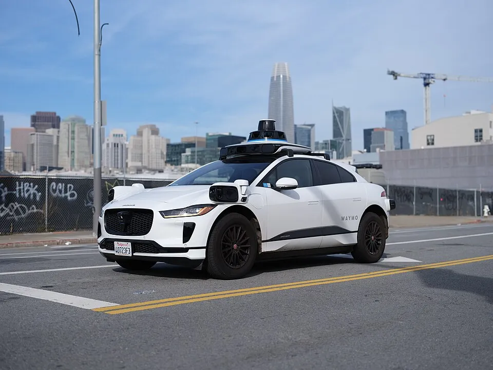 A white Waymo self-driving car with roof sensors on a San Francisco street